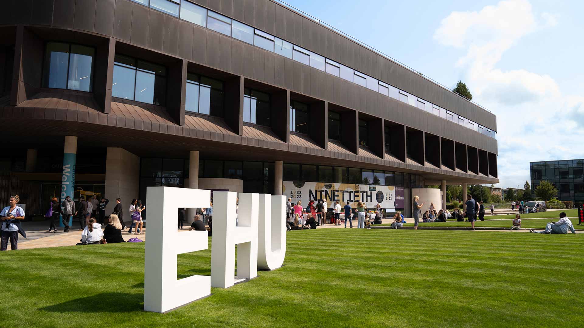 Image of the EHU signage outside of the Catalyst building with visitors on campus.